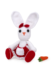 Crochet white rabbit sitting next to a detached handmade orange carrot.