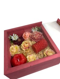 Crimson red wooden gift box with sliding glass lid containing floral-shaped wax candles.