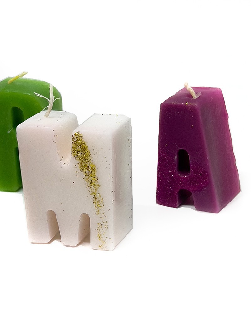 Group of white, green, and purple letter candles with gold glitter accents.