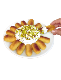 A hand dipping a golden Karabij cookie into fluffy white Natef meringue topped with crushed pistachios.