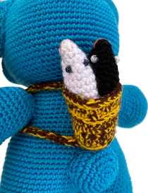 Close-up of a woven miniature basket with a white and black crochet fish inside.