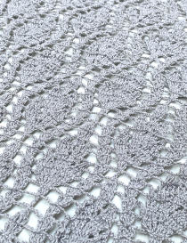 Macro shot of the intricate open-work floral crochet stitch pattern in silver.