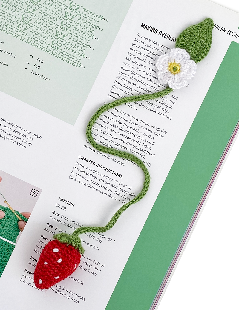 Handmade crochet strawberry bookmark lying on an open craft magazine.
