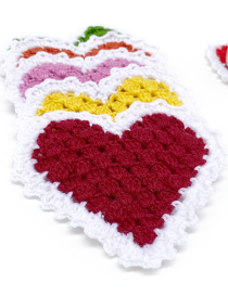 Detailed view of the knit texture and scalloped white edge on a burgundy heart coaster.