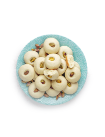 A blue plate filled with homemade Syrian Ghorayeba butter cookies topped with pistachios.