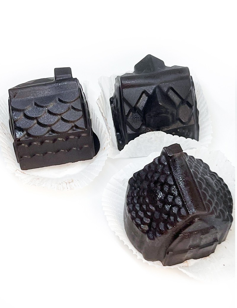 Three dark chocolate treats molded into highly detailed shapes of miniature houses in paper liners.