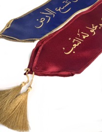 Close-up of maroon and blue satin graduation stoles with gold Arabic calligraphy and tassels.