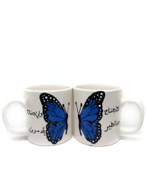 Pair of white ceramic mugs with a blue butterfly design and Arabic calligraphy.